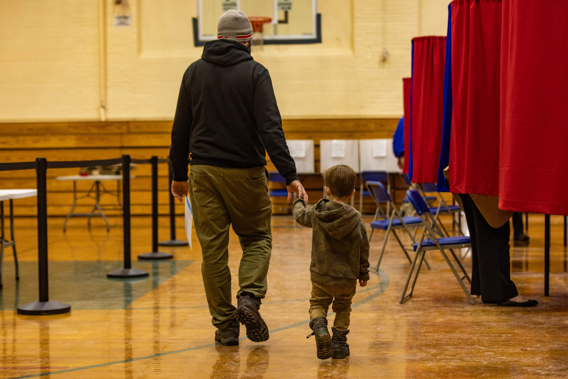 A man, with a ballot in his hand, walks with his son along the aisle of voting booths at the Talbot Gym in Exeter. (Jesse Costa/WBUR)