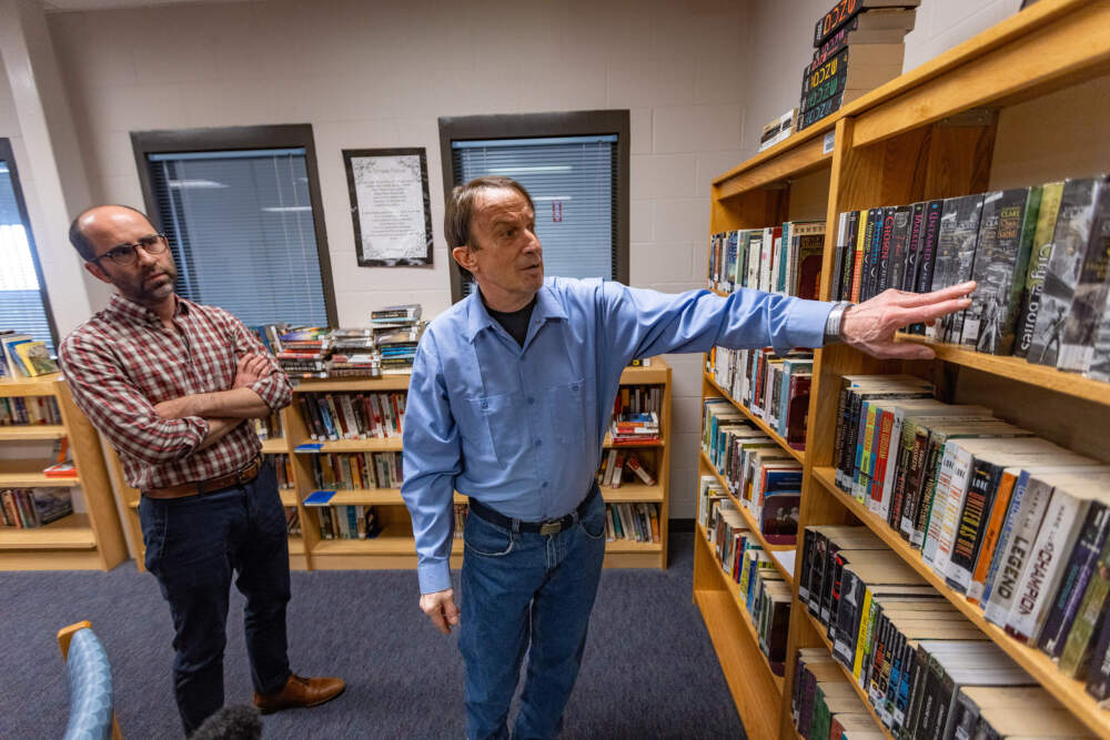 Librarian Brian Stokes looks on as inmate John Sheehan shows how books have been organized by author, making it easier to find the titles he wants. (Jesse Costa/WBUR)
