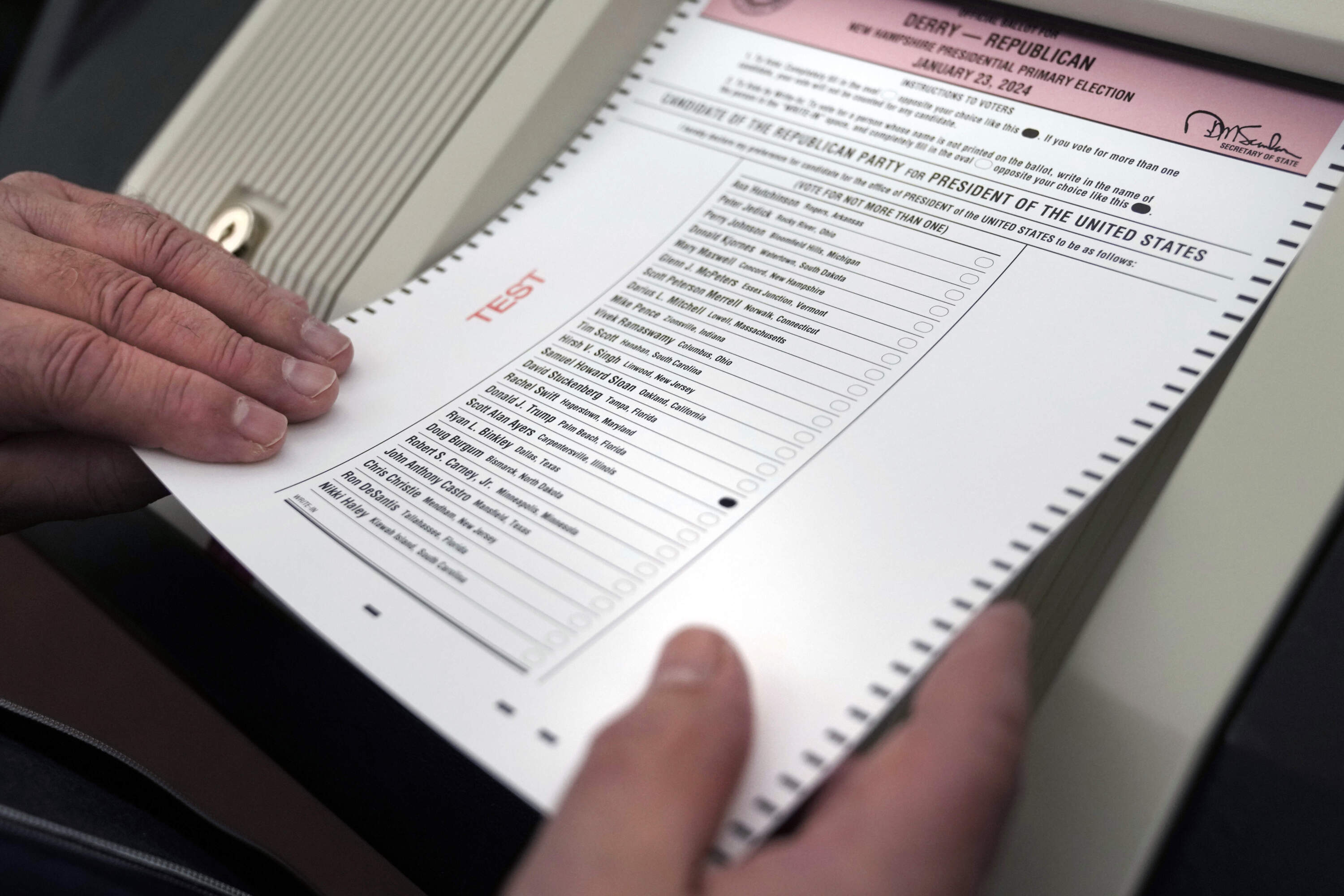 A public witness loads a test ballot into a vote counting machine while testing machines before the New Hampshire primary. (Charles Krupa/AP)