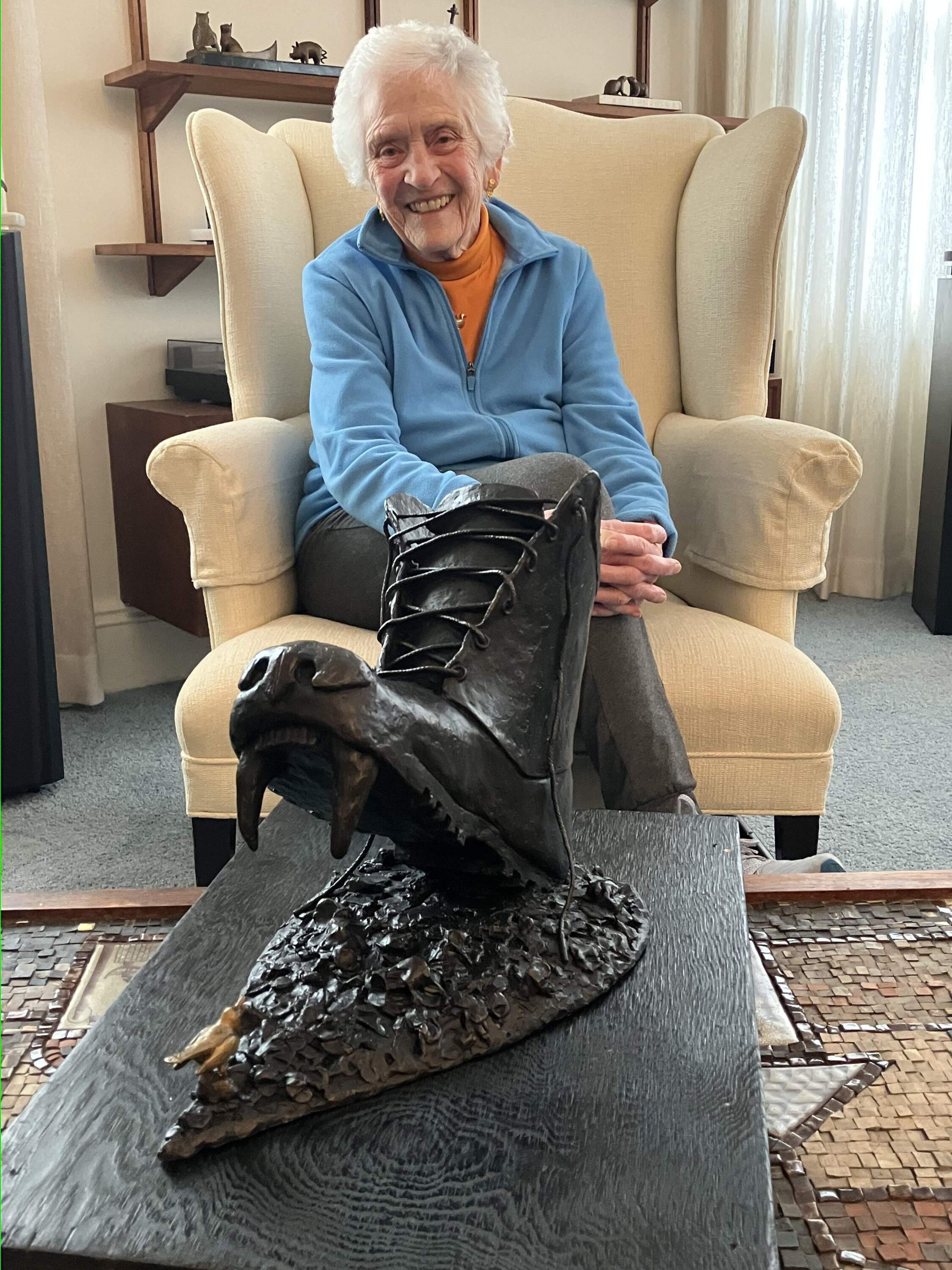 95-year-old Nancy Schon at her Massachusetts home with her sculpture depicting a Russian boot, emblazoned with a bear-face and fangs, crushing a delicate nightingale, the state bird of Ukraine. The bird rests on a tear-shaped pool of rubble. (Karyn Miller-Medzon/Here &amp; Now)