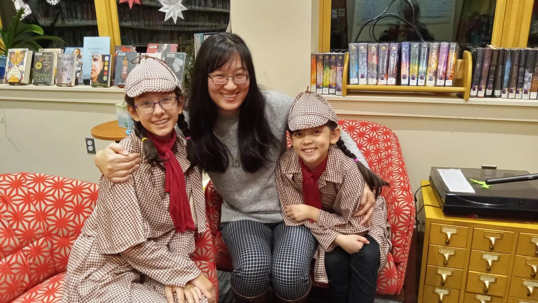 Emma (left) and Belley Barrett (right), with their mother, Cyndi Barrett, at the Hadley Public Library. The sisters read from a book they wrote, "Sister Detectives." It's a mystery for children, in English and Chinese. (Jill Kaufman/NEPM)