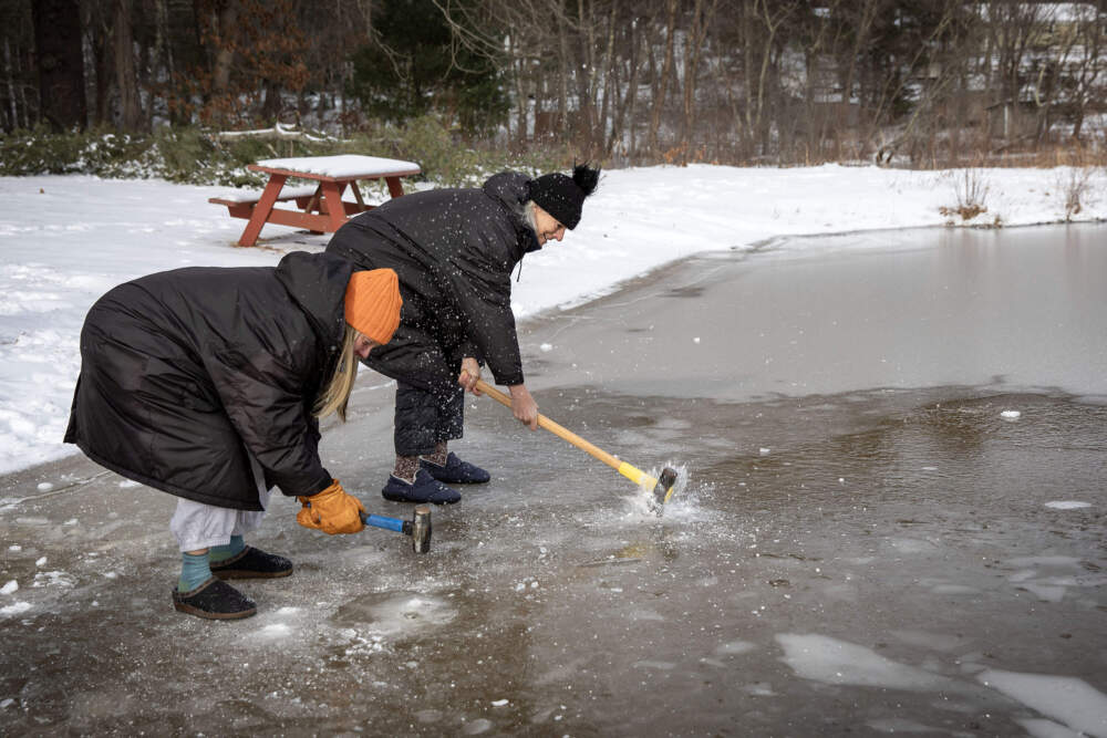 Claire Smith and Cognoscenti contributor Libby DeLana (black hat) start hacking through the ice at Stiles Pond in Boxford. (Robin Lubbock/WBUR)