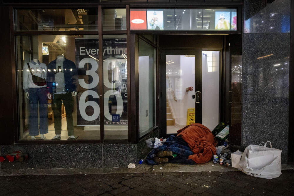A person sleeps under blankets in a store entrance at Boston's Downtown Crossing. (Robin Lubbock/WBUR)