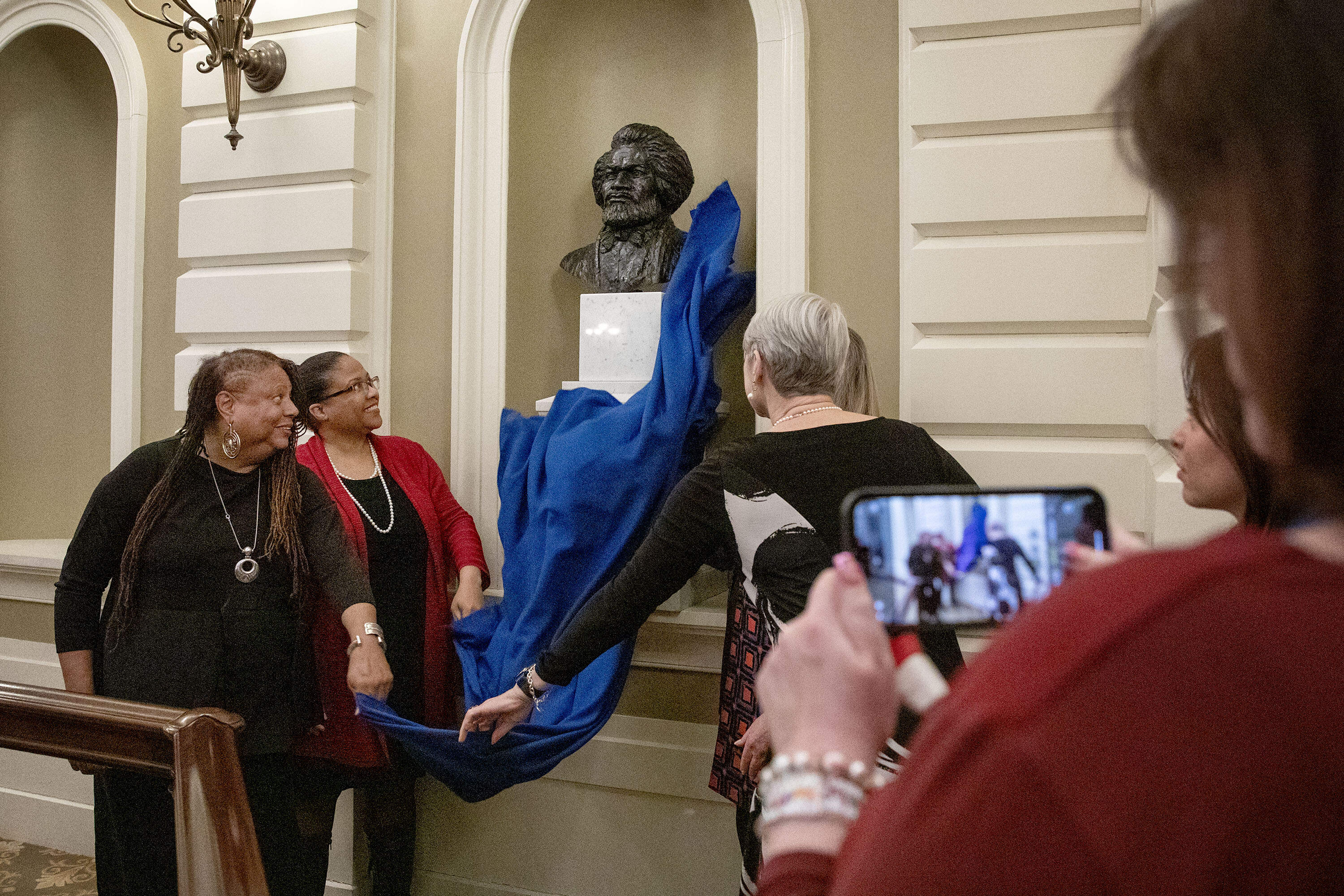 L’Merchie Frazier, Member of the State House Art Commission, Dr. Noelle Trent, President & CEO, Museum of African American History, Senate President Karen E. Spilka and Nina Lillie LeDoyt, daughter of Artist Lloyd Lillie, unveil the bust of Frederick Douglass in the Massachusetts State House Senate Chamber. (Robin Lubbock/WBUR)