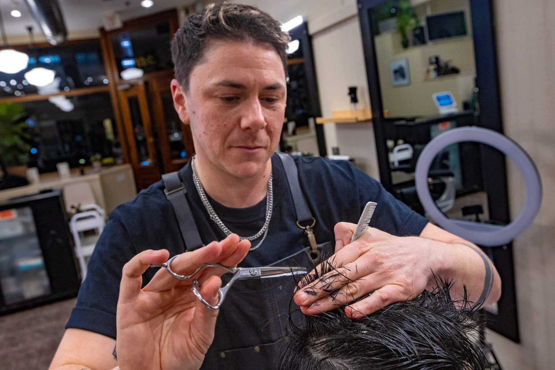 M Arida uses scissors to trim Aaron Chio’s hair. (Jesse Costa/WBUR)