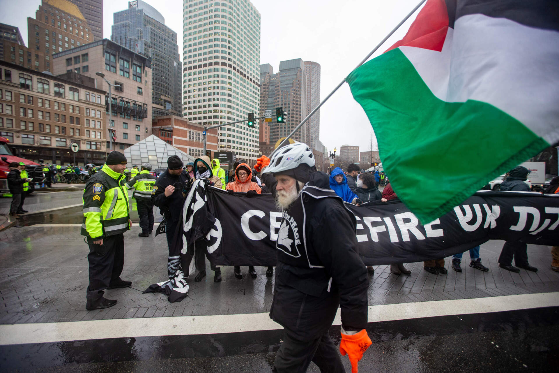 A protester walks through the scene carrying a Palestinian flag as police arrest fellow demonstrators. (Jesse Costa/WBUR)
