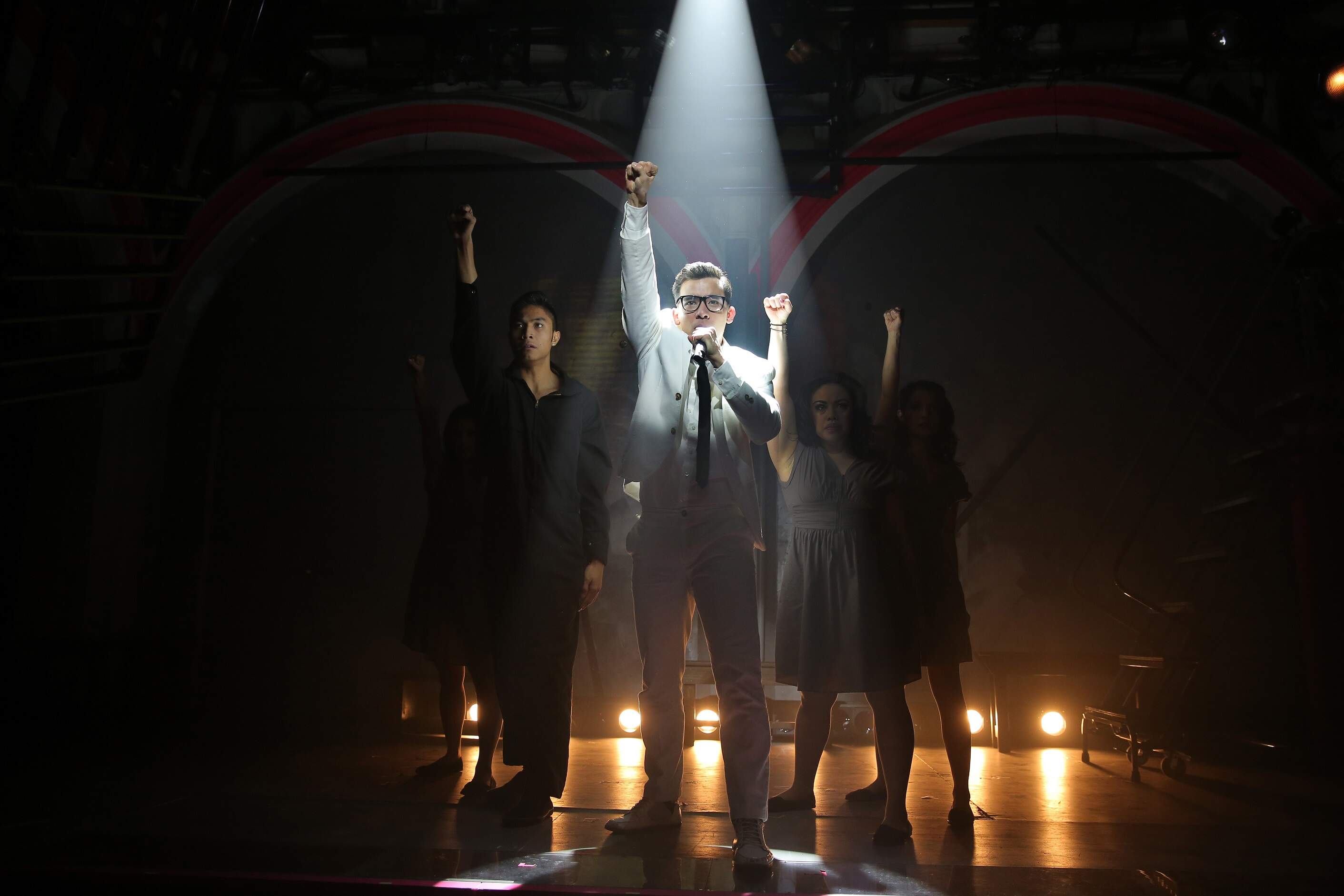 Conrad Ricamora under spotlight and the cast of "Here Lies Love" at the Public Theater. Some critics were known to pump their fists along with Benigno Aquino, Jr. (Courtesy Joan Marcus)