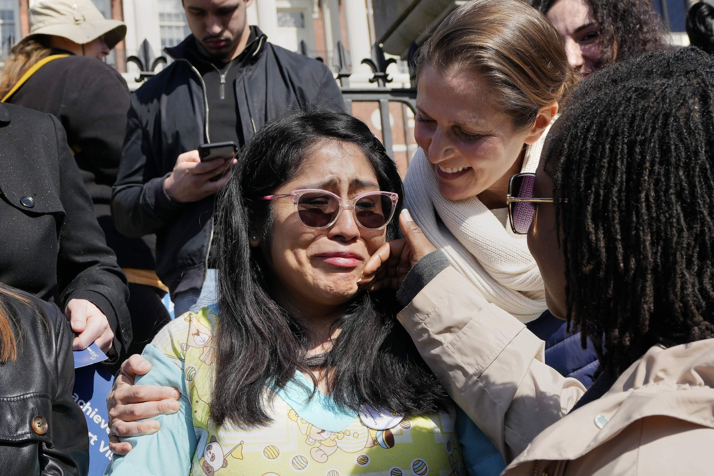 Alejandra De La Cruz, left, a lead toddler teacher at Ellis Early Learning reacts after speaking during a rally outside the State House. (Michael Dwyer/AP)
