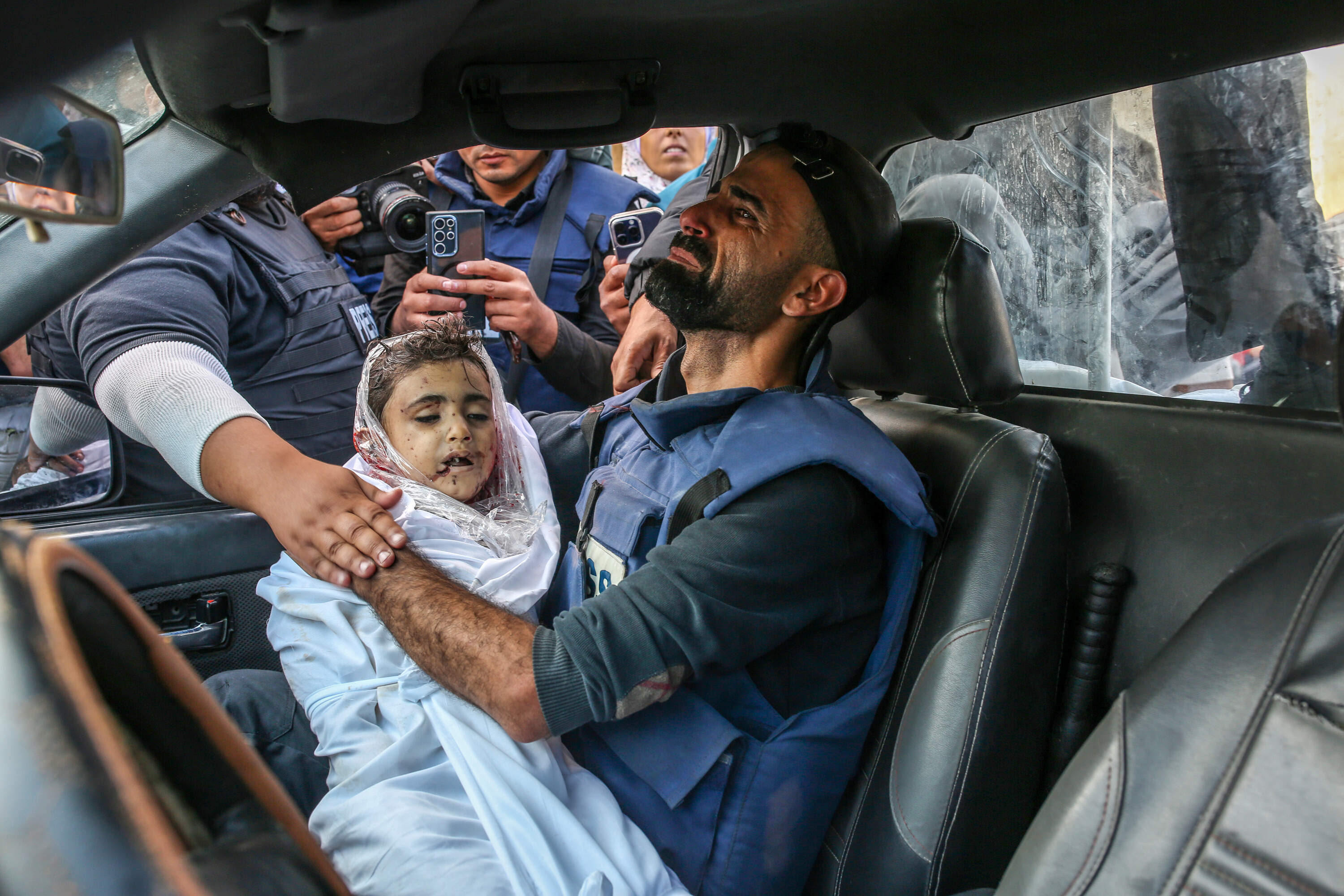 The photojournalist Mohammed al-Aloul holding the body of one of his children killed in the war. (Samar Abu Elouf/New York Times)