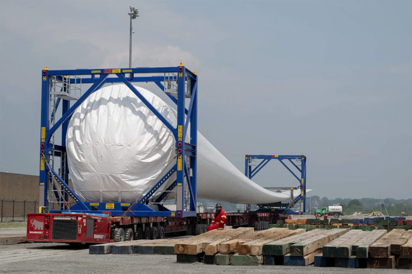 Workers help transport an offshore wind turbine blade before it is stacked on top of another at Vineyard Wind on June 8, 2023, in New Bedford, Massachusetts. (Raquel C. Zaldívar/New England News Collaborative)