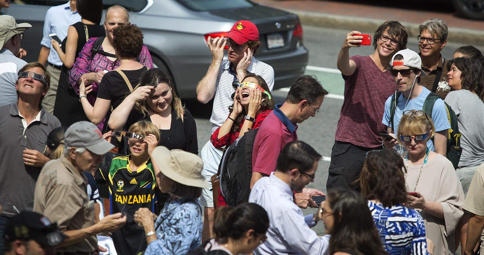 On the sidewalk in front of the Boston Public Library, people share protective glasses so they can look up during a 63% partial solar eclipse in 2017. (Robin Lubbock/WBUR)