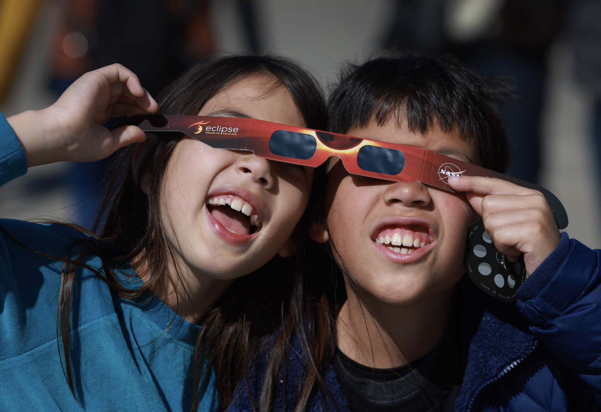 Miriam Toy and Oliver Toy share a pair of eclipse glasses that NASA was handing out as they await the eclipse on April 08, 2024, in Houlton, Maine. (Joe Raedle/Getty Images)