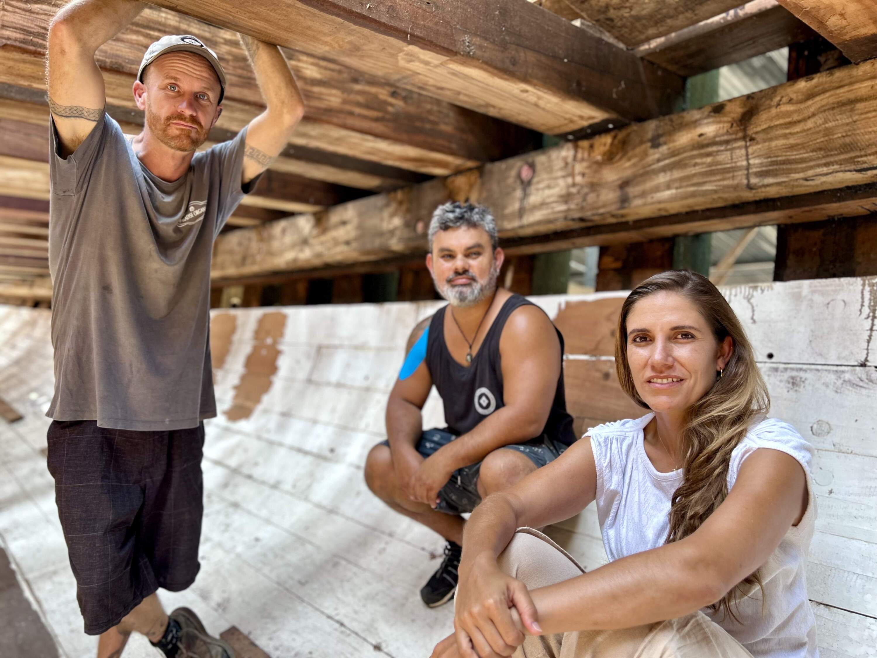 Co-founders John Porras, Lynx Guimond (left) and staff member Alejandra Terán pictured inside the cargo hold of Ceiba, a 3-masted top-sail schooner under construction in Costa Rica. (Peter O'Dowd/Here &amp; Now)