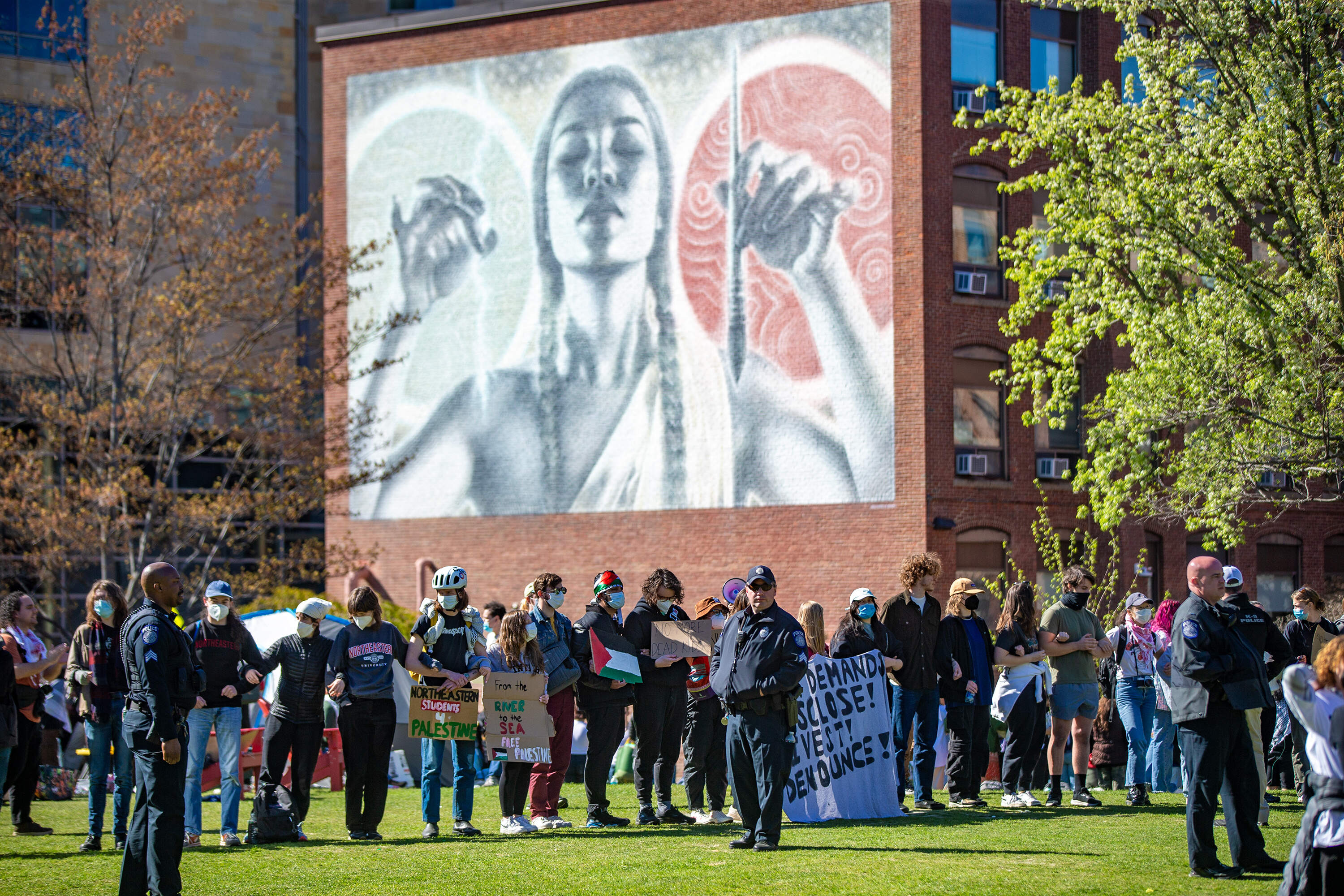Campus police watch as while protesters chant surrounding the encampment at Centennial Common at Northeastern University. (Jesse Costa/WBUR)