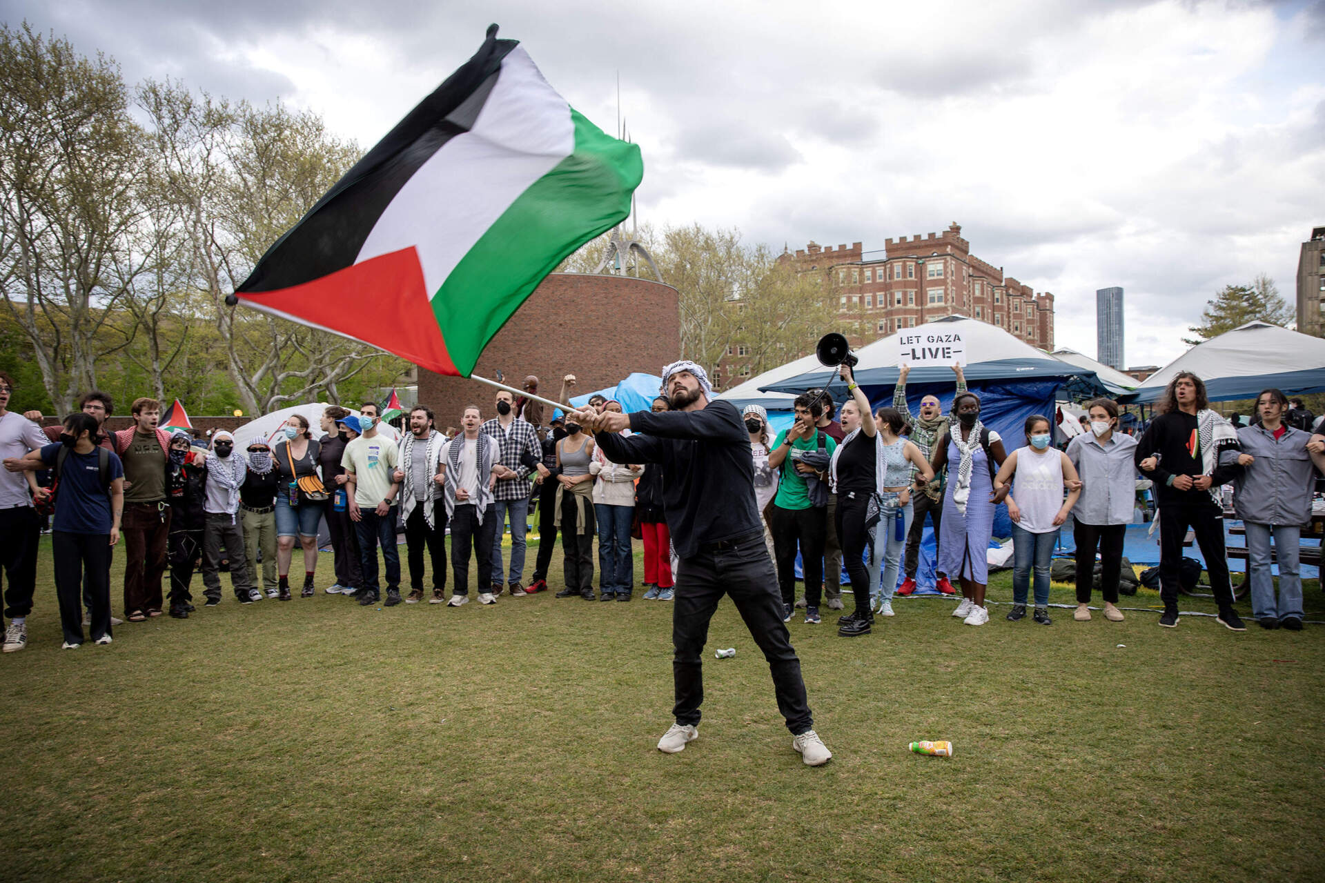 A protester waves a Palestinian flag after demonstrators re-occupy the encampment on MIT's Kresge Lawn. (Robin Lubbock/WBUR)