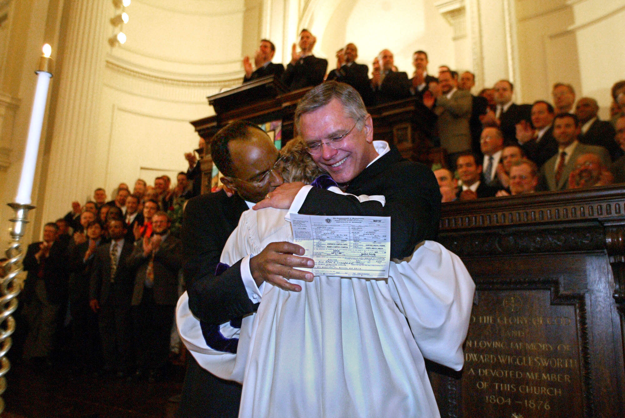 David Wilson (left) and Robert Compton hug the Rev. Kim Crawford Harvie after she signed their marriage certificate following the ceremony at Arlington St. Church. The Boston Gay Men's Chorus is in the background. (John Wilcox/MediaNews Group/Boston Herald via Getty Images)