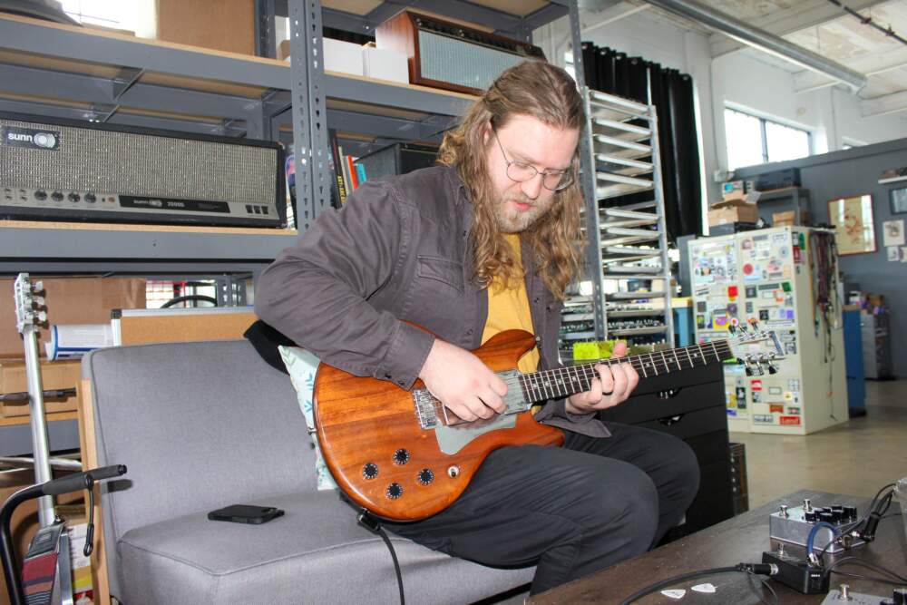 John Snyder plays the guitar and tests out a pedal. (Lukas Harnisch for WBUR)