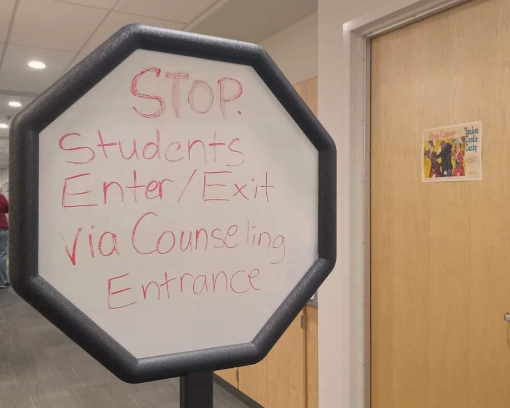 A sign in the front office the high school in West Springfield, Massachusetts, keeps traffic flowing. At the other end of the hall, two seniors are stationed at a table, answering a variety of student questions. (Jill Kaufman/NEPM)