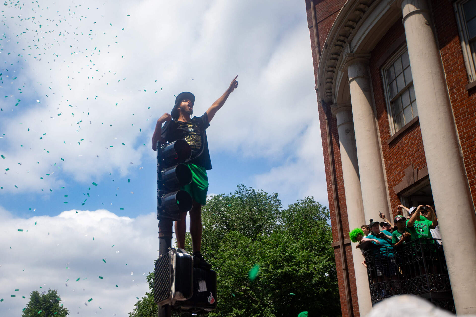 A fan stands atop a walk signal during the Celtics championship parade. (Jesse Costa/WBUR)