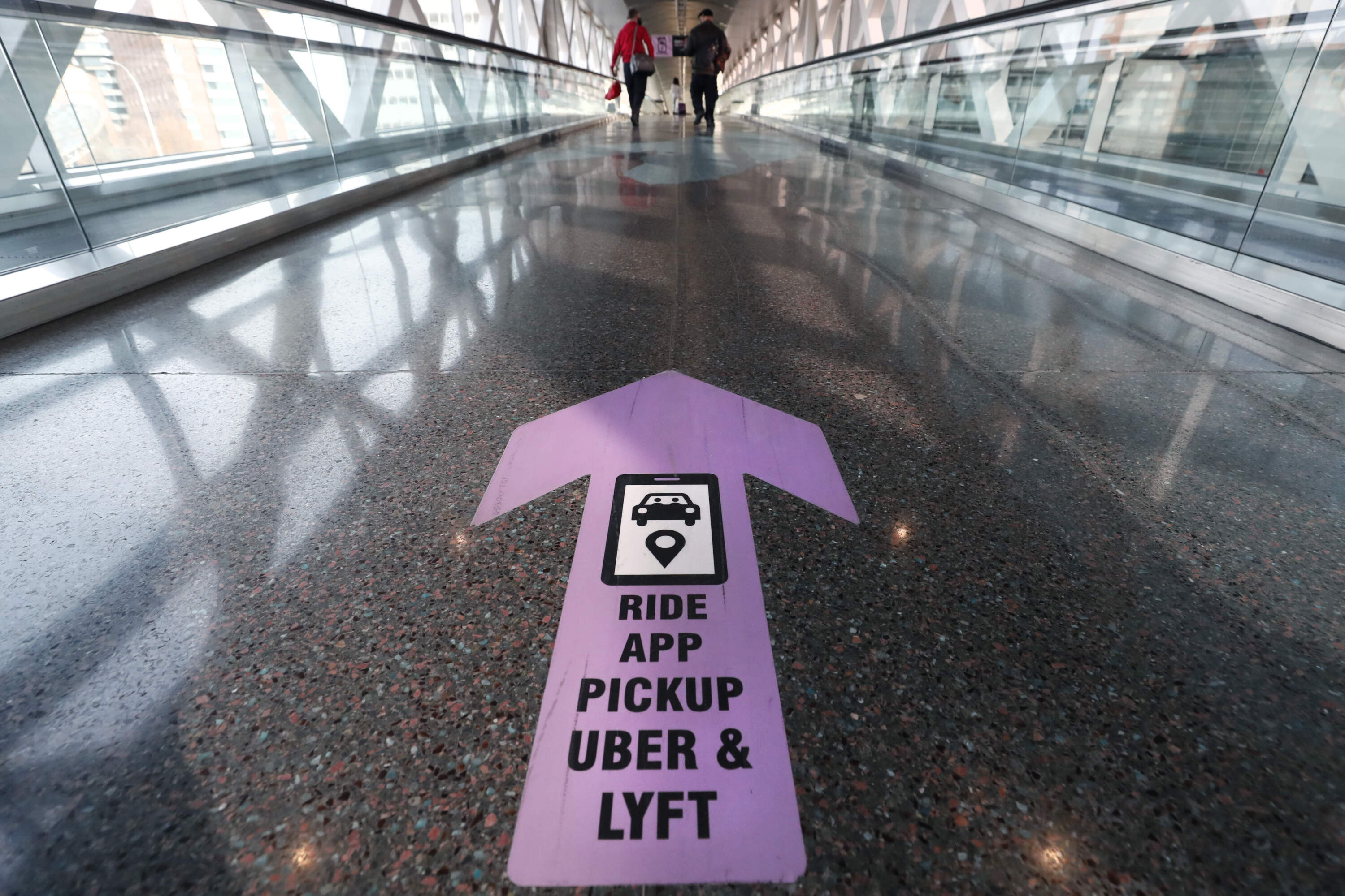 Travelers walk across a skyway bridge towards the Uber and Lyft shared ride pickup point at Logan Airport in Boston. (Michael Dwyer/AP)