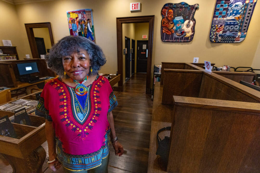 Artist Susan Thompson standing in the Hyde Park branch of the Boston Public Library where her exhibit of quilts, “Go Down to the River and Talk to ‘JAH’,” are on display. (Jesse Costa/WBUR)