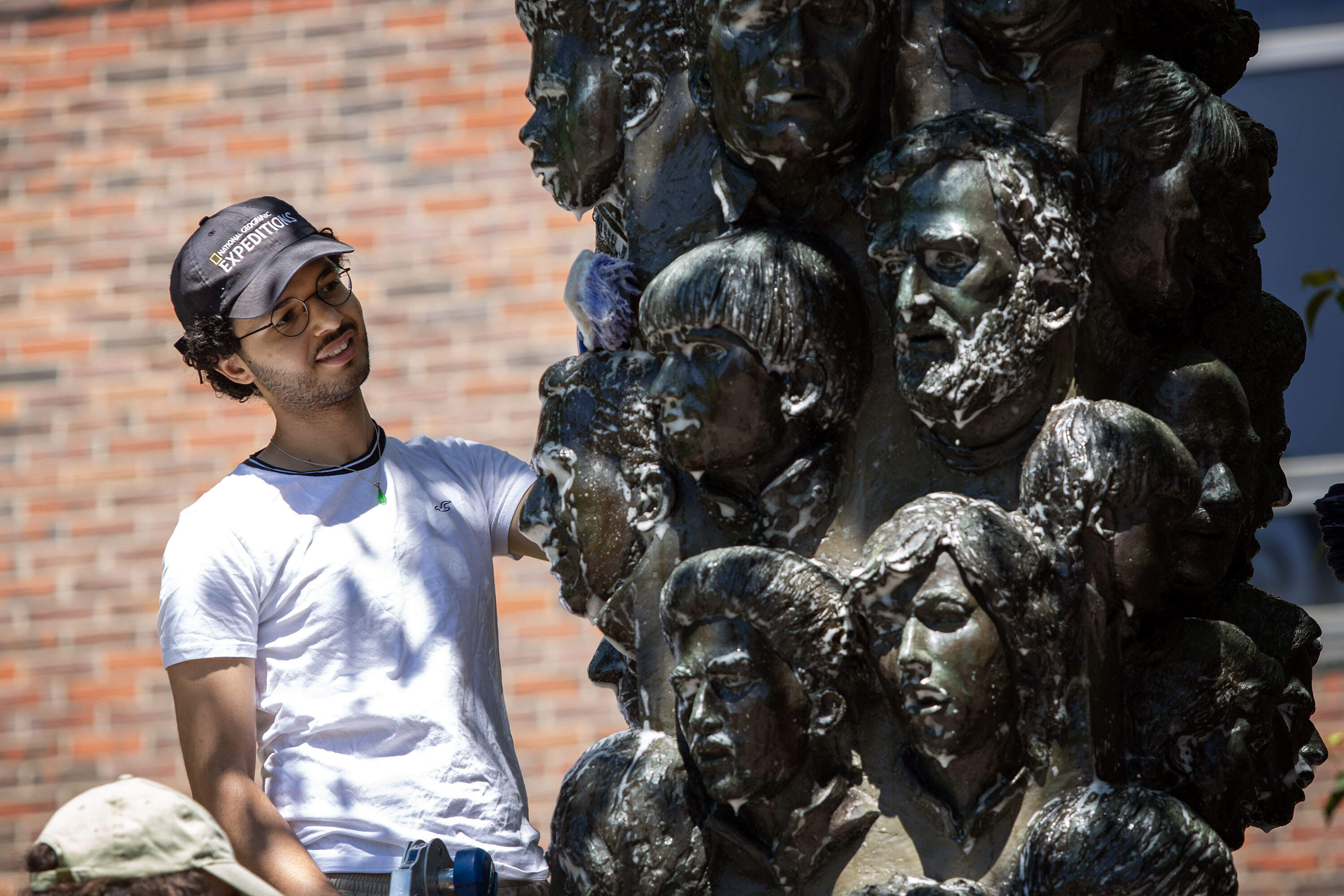 Oussama Ouadani, a data and arts collection specialist for Cambridge, scrubs sculptor James Tyler's "Tower of East Cambridge Faces." (Robin Lubbock/WBUR)