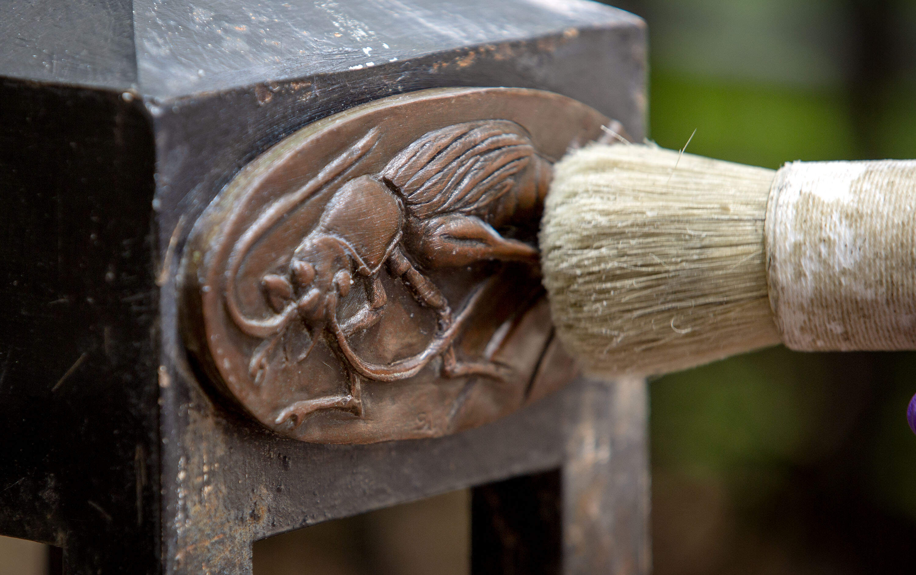 An insect medallion sculpture by Nancy Webb at Charles Park gets a coat of bowling alley wax. (Robin Lubbock/WBUR)