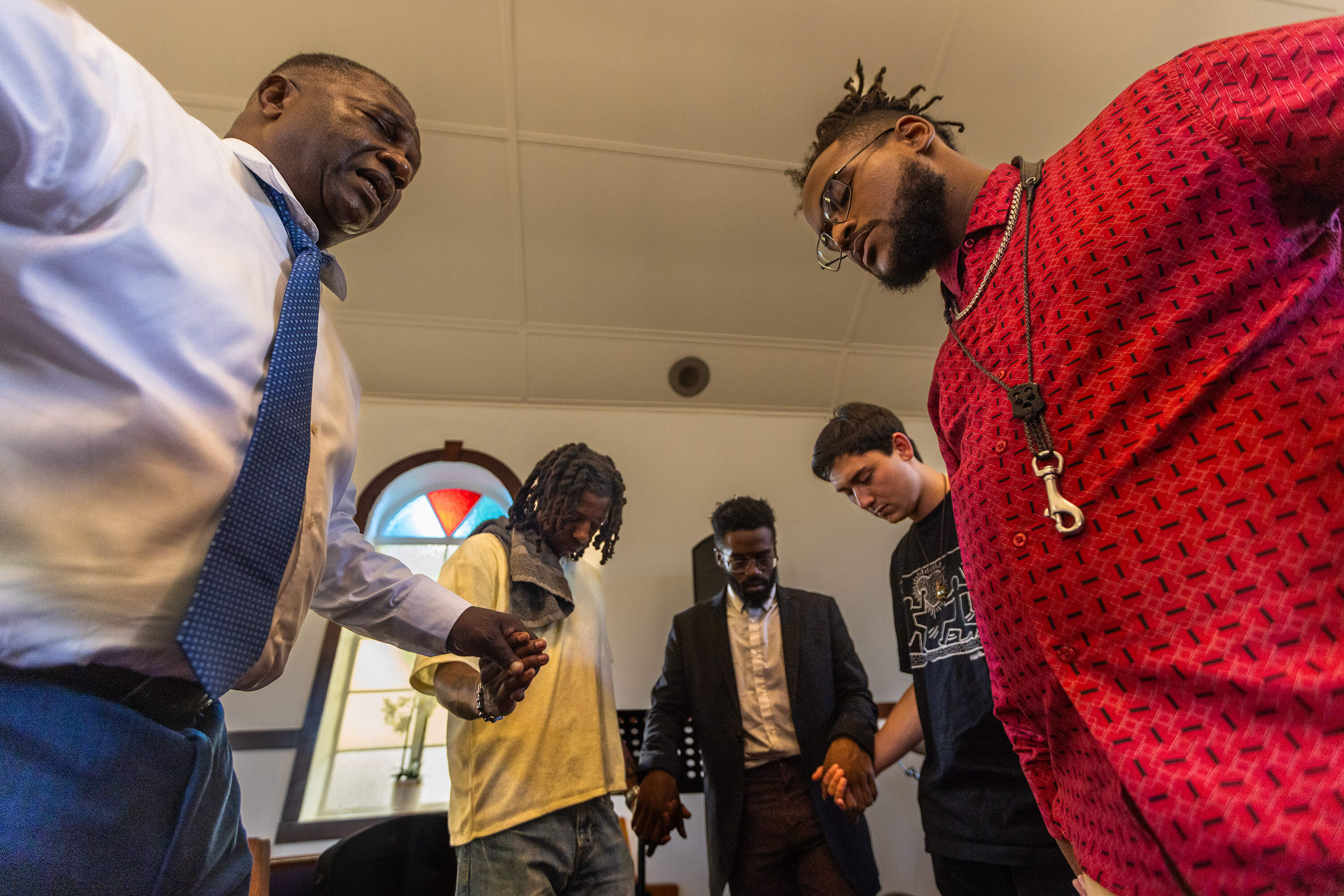 Reverend Miniard Culpepper, left, says an opening prayer with, (l-r) drummer Christian Napoleon (aka Napo), guitarist Christopher Hammond II, keyboardist JT Ho-Mueller and saxophonist Seventh Sun, before the group rehearses at the Pleasant Hill Baptist Church in Dorchester. (Jesse Costa/WBUR)