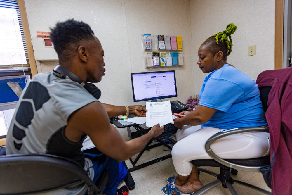 Destin Jean Baptiste, left, has been waiting for weeks to get his work papers, which appear to be lost in the mail. Fedelyne Maurice helps him navigate the process at the Whittier Street day center. (Jesse Costa/WBUR)