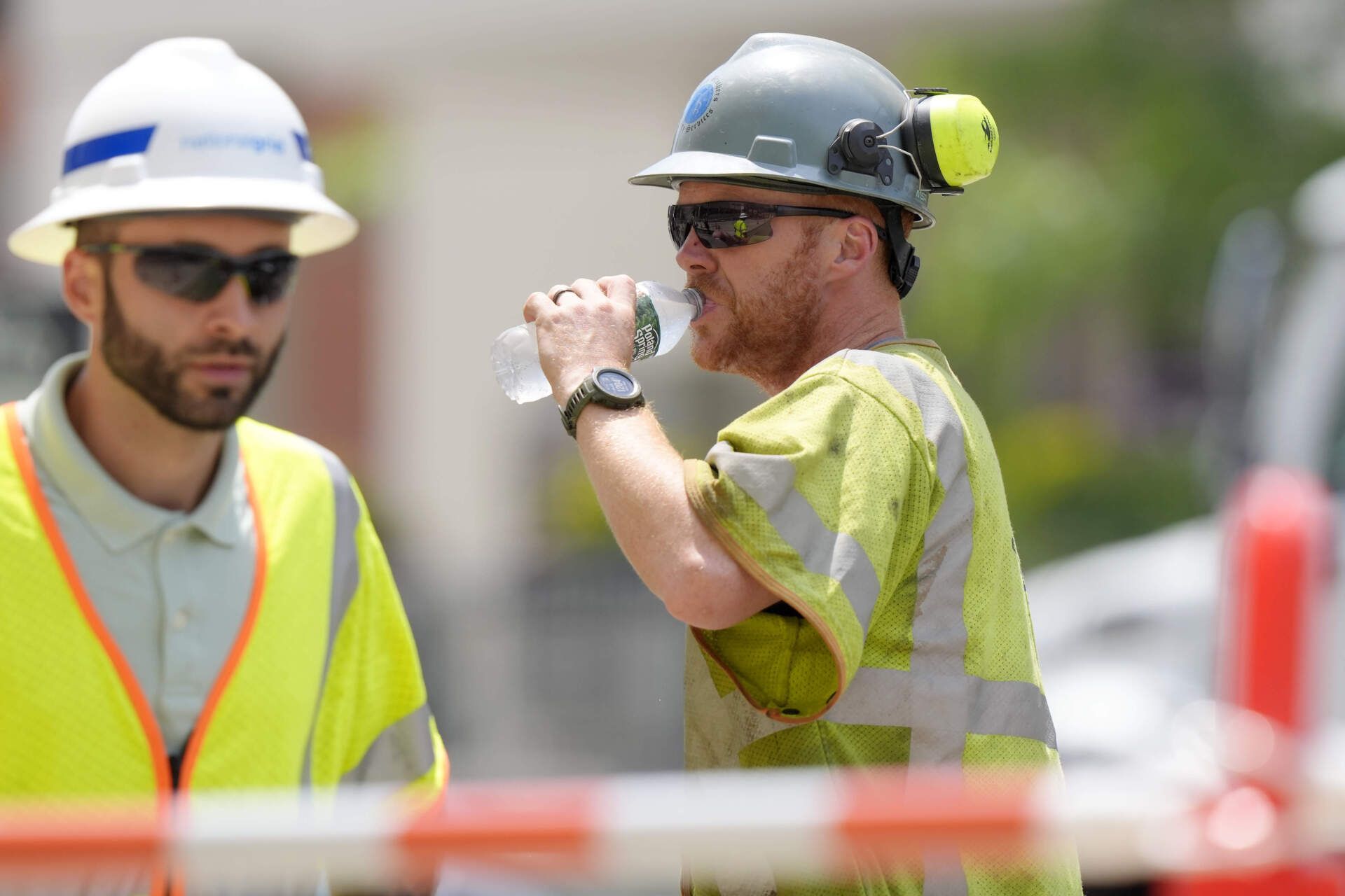 A worker, right, takes a drink of water while working in temperatures above 90 degrees at a gas line work site in Boston. (Steven Senne/AP)