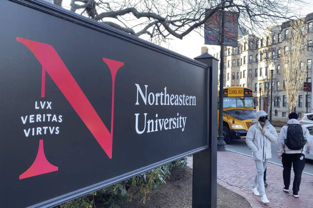 Pedestrians walk near a Northeastern University sign on the school's campus in Boston. (Rodrique Ngowi/AP)
