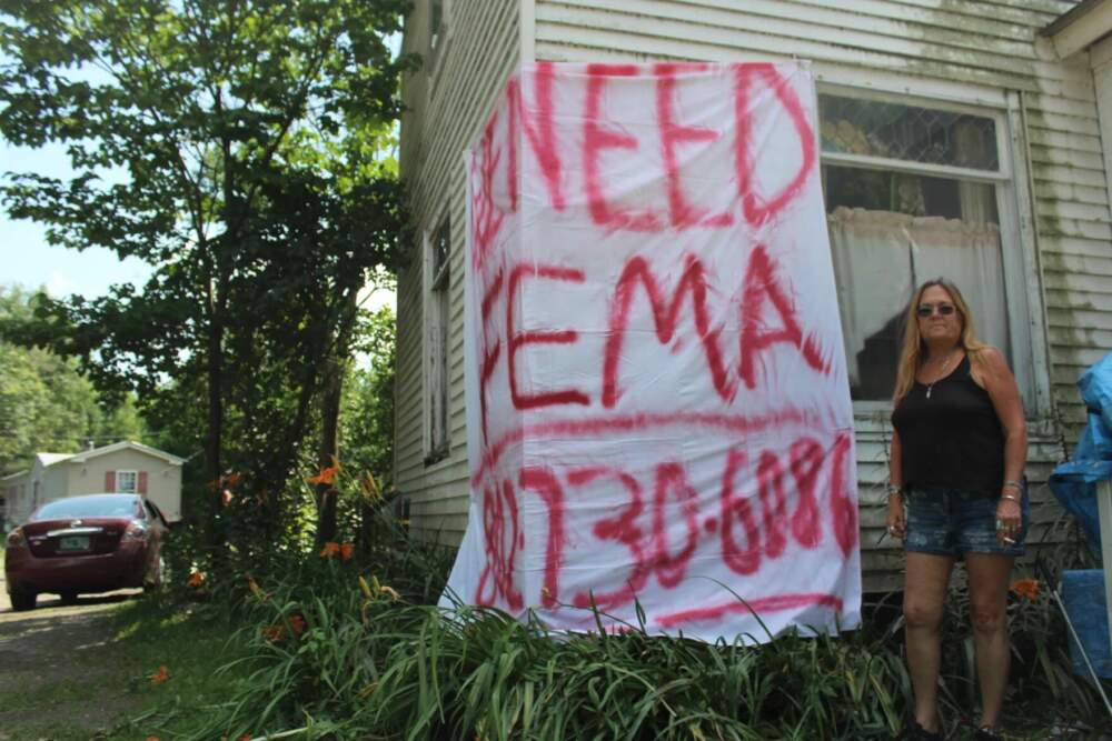 Tosh Gilmore of Johnson stands in front of her flooded house on July 13, 2023. She made this sign, hoping someone from FEMA might see it. (Abagael Giles/Vermont Public)