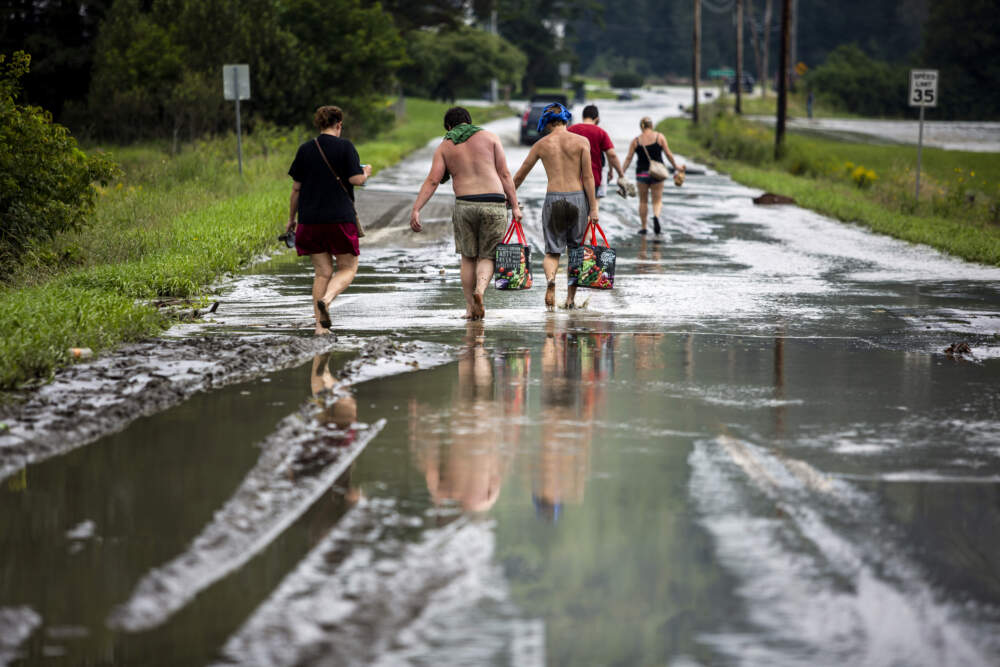 Residents walk barefoot away from flood damage in Vermont. (Dmitry Belyakov/AP)