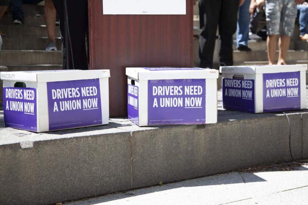 Boxes of voter signatures sit in front of the podium at a July 2, 2024 press conference about a ballot question that would give Uber and Lyft drivers the right to unionize. (Chris Lisinski/SHNS)
