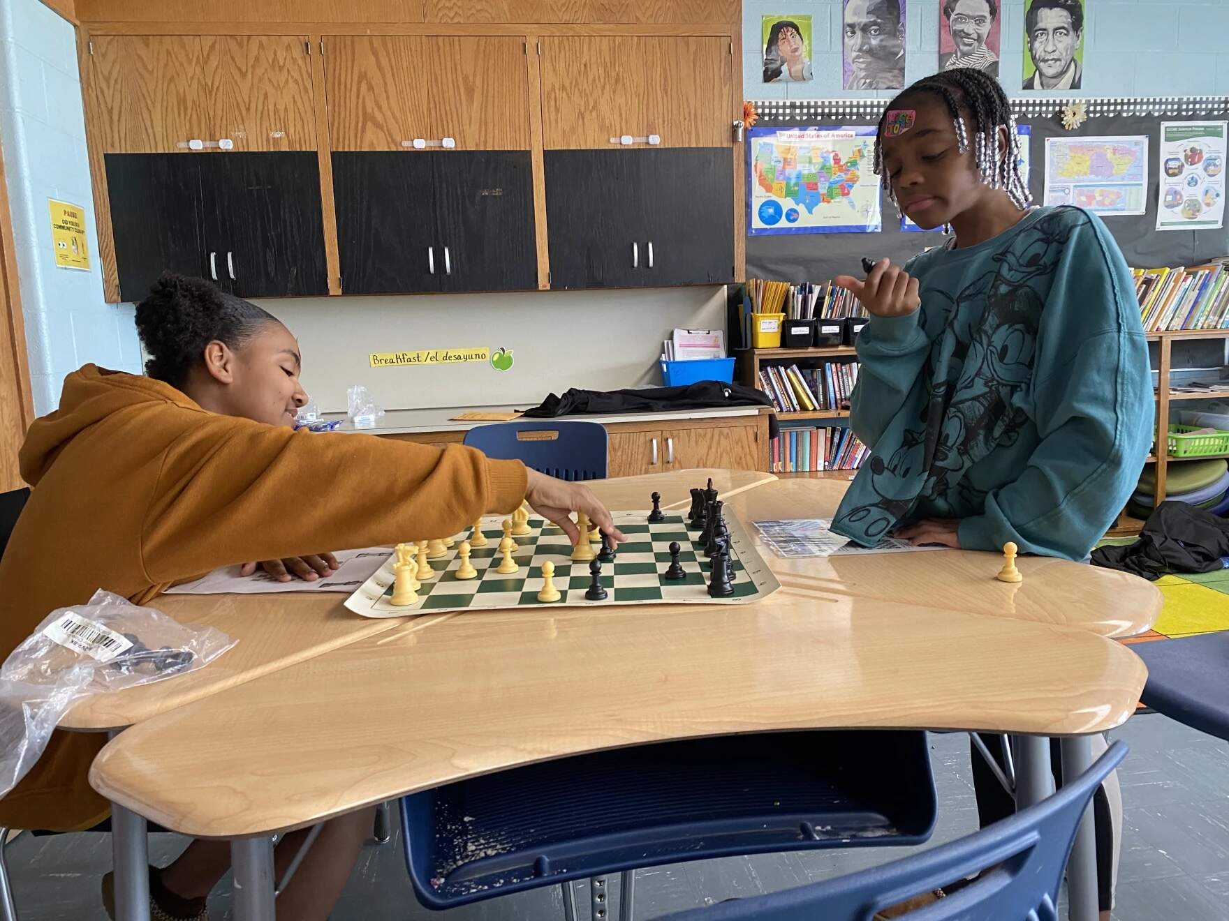 Two fifth graders sit across from each other at a desk, a chess board between them. Nicole Davis, left, and Tae'la Feliciano are both members of the Cheetah Chess Club at McMahon Elementary School in Holyoke, Massachusetts. In this picture, they play chess against each other on May 2, 2024. (Dusty Christensen/NEPM)