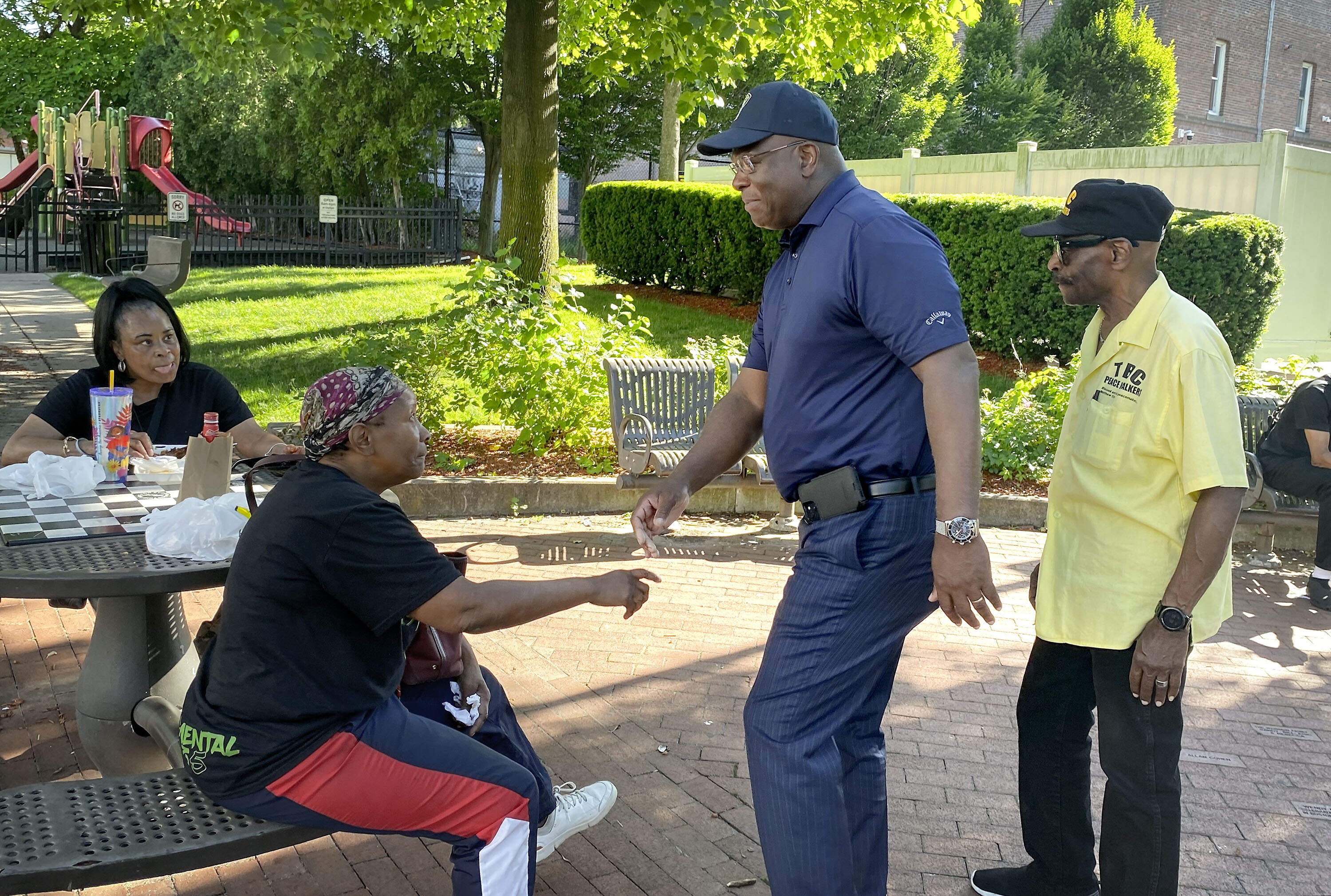 Boston Police Commissioner Michael Cox greets people sitting in a park in Roxbury while out on a recent community outreach "peace walk" this summer. (Deborah Becker/WBUR)