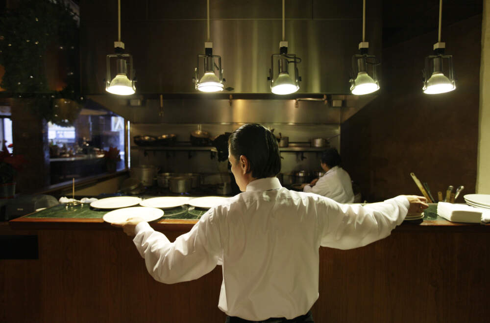 A waiter reaches for plates at a restaurant. (Eric Risberg/AP)