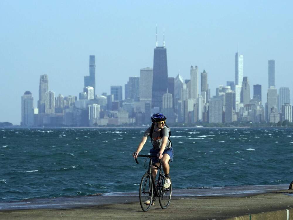 A person rides a bike on a breakwater along Lake Michigan against downtown skyline in Chicago. (Kiichiro Sato/AP)