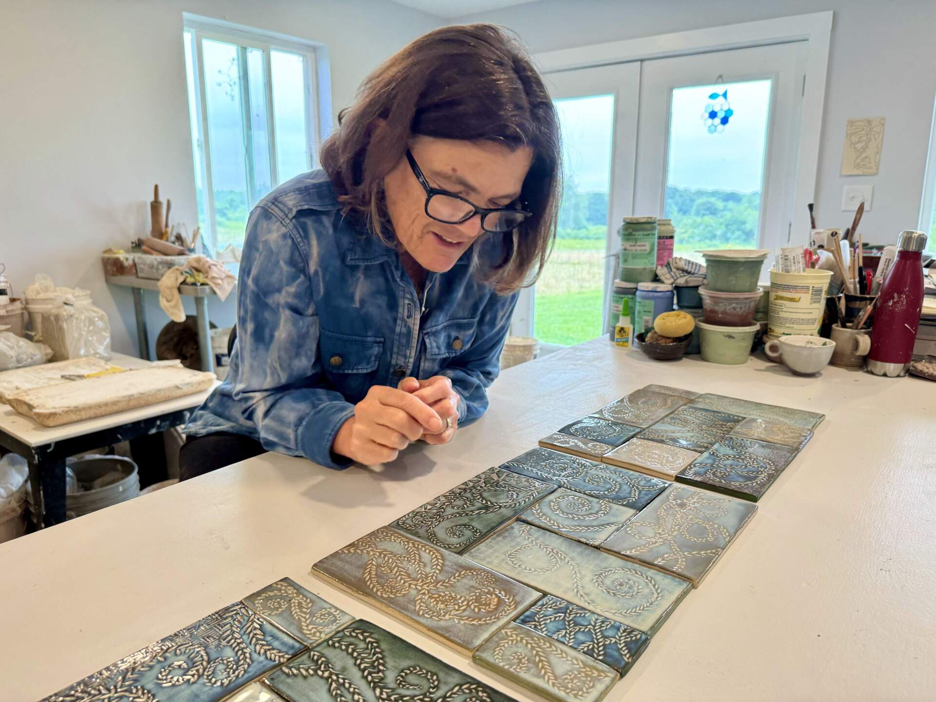 Cali Almy looking at the ceramic tiles she made for a commission at UMass Memorial Hospital in Worcester. (Photo by Maddie Browning)