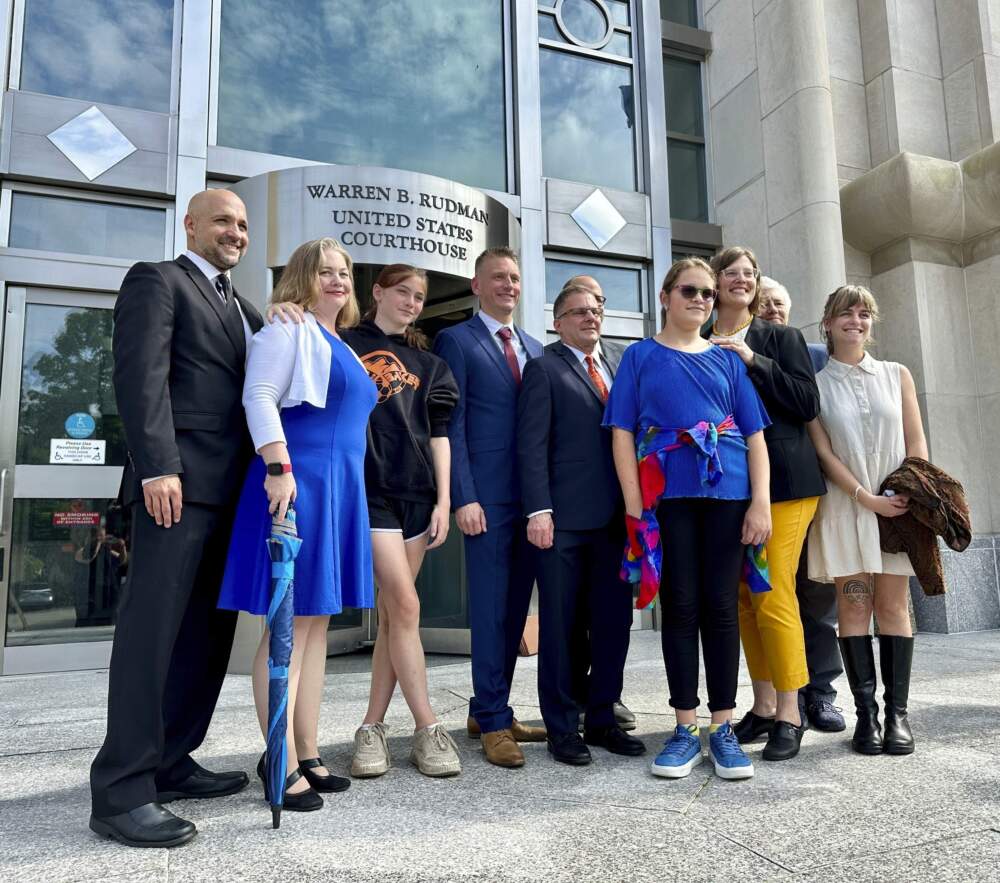 Two teens challenging New Hampshire's new law banning transgender girls from girls' sports teams, Parker Tirrell, third from left, and Iris Turmelle, sixth from left, pose with their families and attorneys in Concord, N.H., Monday, Aug. 19, 2024. (Holly Ramer/AP)