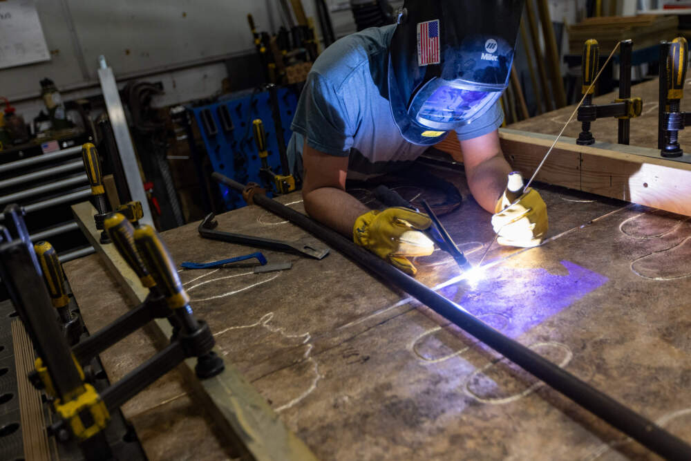 Sincere Metal Works welder TJ Sadowski begins welding the bronze panels of Nancy Schon’s “Noble Journey Sculpture” to create one piece. (Jesse Costa/WBUR)