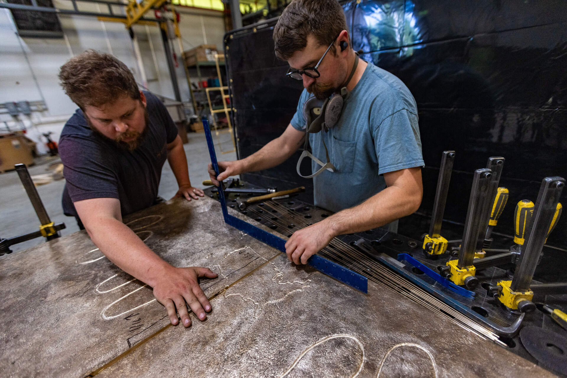 Sincere Metal Works owner Dan Kendall and welder TJ Sadowski line up the four bronze panels of Nancy Schön's “The Noble Journey," before welding them together. (Jesse Costa/WBUR)