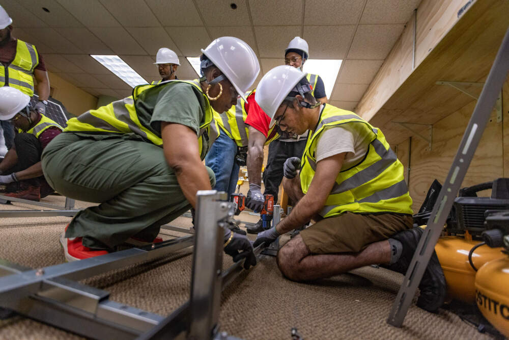 Students Narkeisha Gilbert and Lhoucine Bouhaddou prepare a solar array frame for fastening. (Jesse Costa/WBUR)