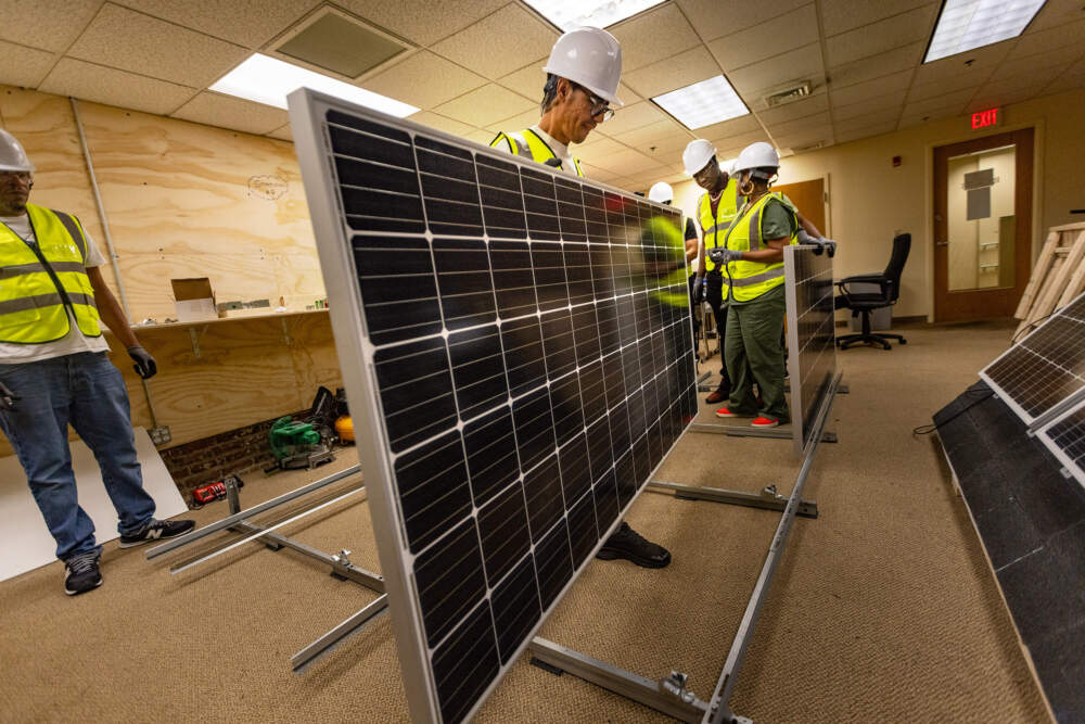 Student Lhoucine Bouhaddou moves a solar panel into place on a rack during the SHINE class. (Jesse Costa/WBUR)