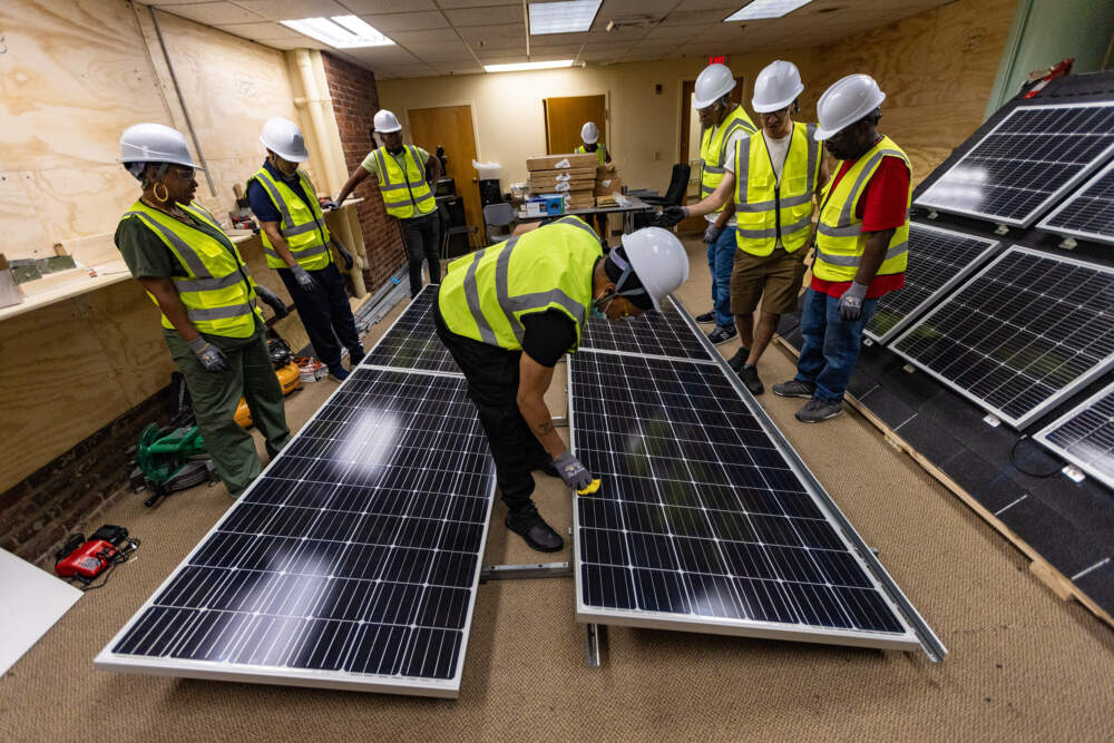 Rashawn Skinner wipes down the solar panels after he and his fellow students finish setting them up. (Jesse Costa/WBUR)