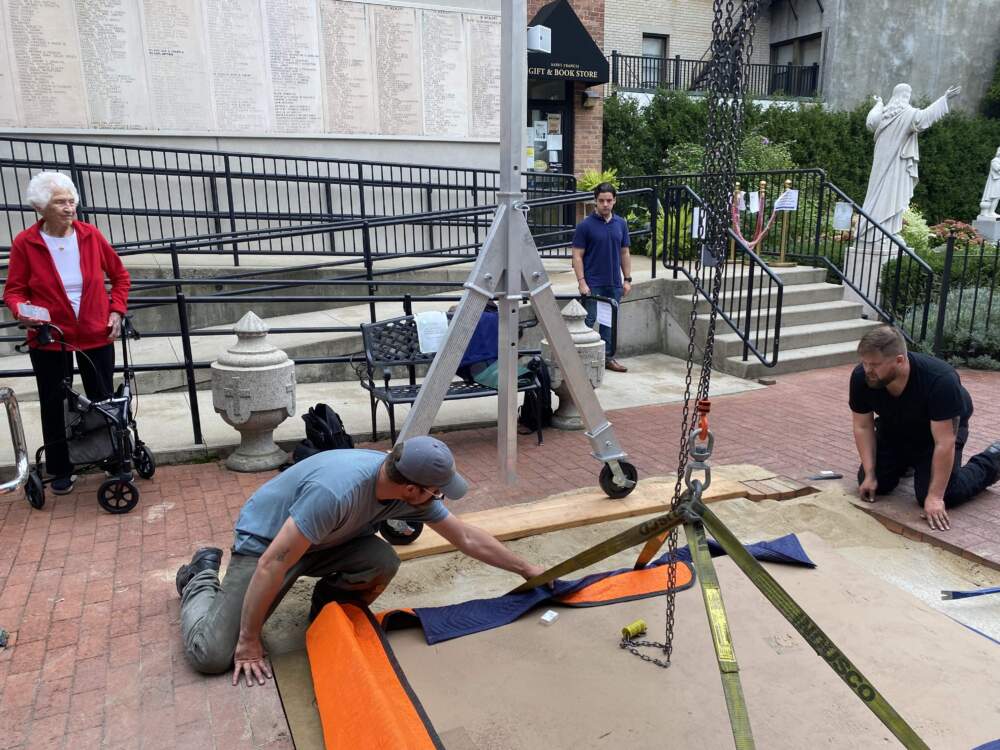 Workers install the sculpture outside of St. Leonard's in the North End. Nancy Schön looks on eagerly. (Andrea Shea/WBUR)