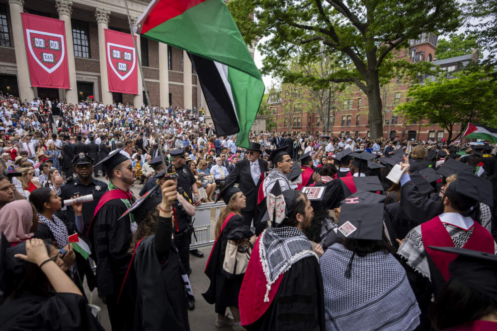 Graduating students hold Palestinian flags and chant as they walk out of Harvard's May 23 commencement in protest over the 13 students who have been barred from graduating due to protest activities. (Ben Curtis/AP)