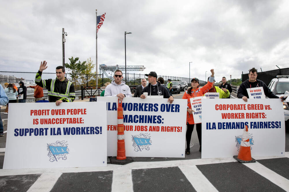 Striking dockworkers from the International Longshoremen’s Association wave at passing vehicles as they block the entrance to the Conley Container Terminal in Boston on Oct. 1, 2024. (Robin Lubbock/WBUR)