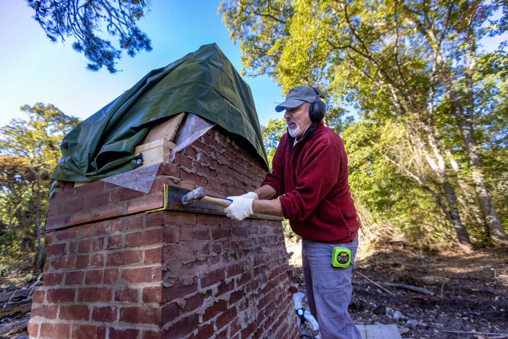Stone mason Conrad Languth carves a column into the fireplace, beneath where the Norman Lewis mural is located. He will install and weld metal bars into the brick in the hopes of lifting the section of fireplace with a forklift without damaging the art piece. (Jesse Costa/WBUR)
