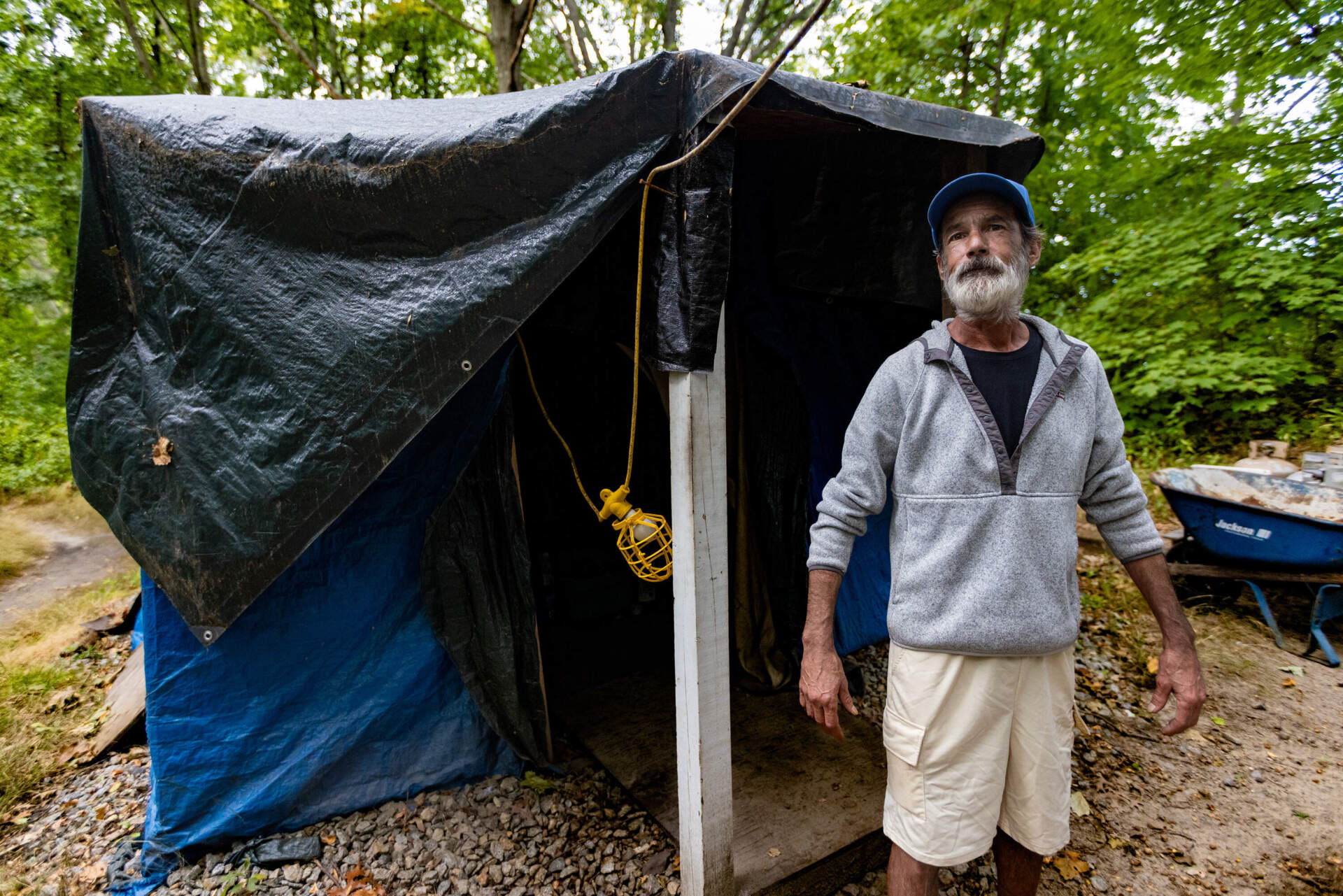 Michael Mello stands the shack he built five years ago in some woods along the Merrimack River in Lowell. "Three rooms — with a porch. And a latrine," he said with a chuckle. (Jesse Costa/WBUR)